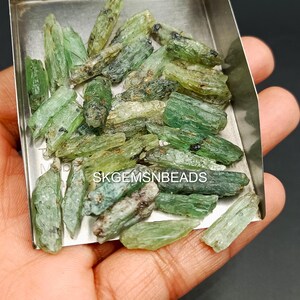 May include: A collection of green and black gemstone rough, also known as green apatite, in a metal tray. The rough is in various sizes and shapes. The rough is ready to be cut and polished into gemstones.