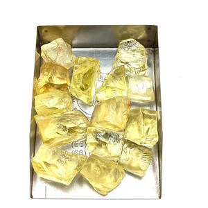 K&ouml;nnte beinhalten: Eine Sammlung gelber, facettierter, roher Edelsteine in einer Metallschale. Die Edelsteine sind in verschiedenen Gr&ouml;&szlig;en und Formen.