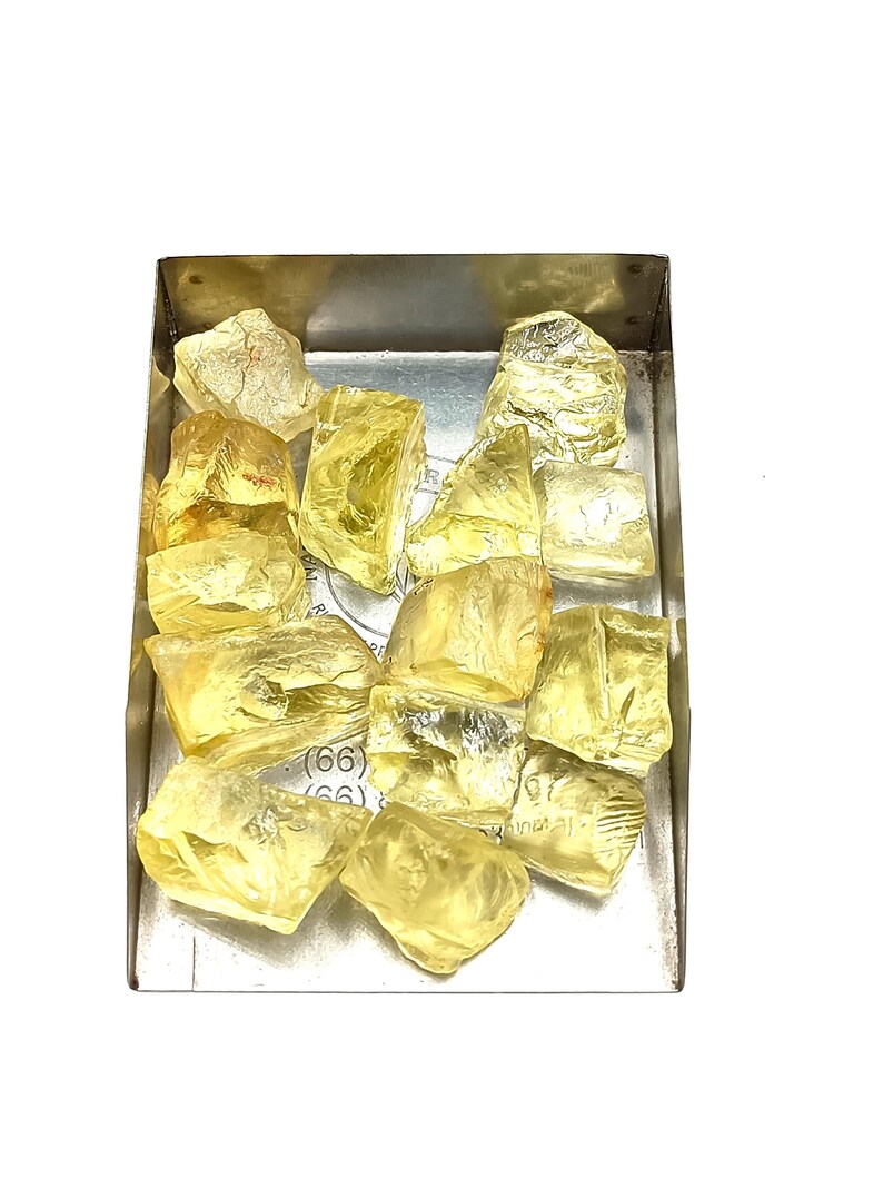 K&ouml;nnte beinhalten: Eine Sammlung gelber, facettierter, roher Edelsteine in einer Metallschale. Die Edelsteine sind in verschiedenen Gr&ouml;&szlig;en und Formen.