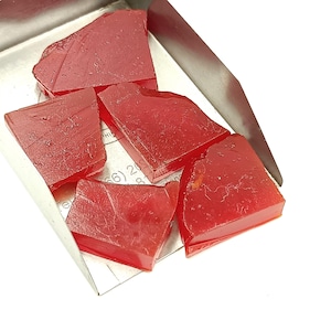 Könnte beinhalten: Fünf Stücke rohe rote Edelsteine in einer Metallschale. Die Edelsteine sind unregelmäßig geformt und haben eine durchscheinende Optik.