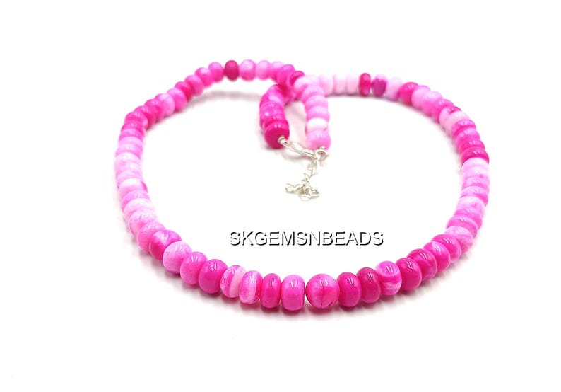 May include: A necklace composed of pink and white beads, with a gradient effect from light to dark. The beads are strung together with a silver clasp. The text "SKGEMSNBEADS" is visible.