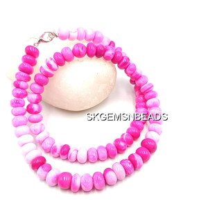 May include: A necklace made of pink and white beads. The beads are a mix of solid pink and pink and white striped. The necklace is displayed on a white surface. The necklace is secured with a silver clasp. The text "SKGEMSNBEADS" is visible.