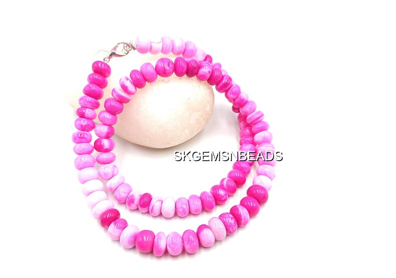 May include: A necklace made of pink and white beads. The beads are a mix of solid pink and pink and white striped. The necklace is displayed on a white surface. The necklace is secured with a silver clasp. The text "SKGEMSNBEADS" is visible.
