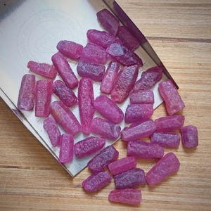 Puede incluir: Una colección de piedras de rubí en bruto de color rosa, con una variedad de formas y tamaños, expuestas en una bandeja de plata.