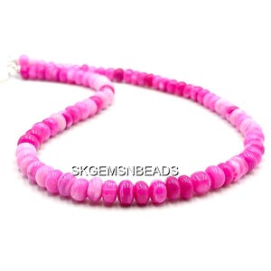 May include: A necklace composed of small, rounded beads in shades of pink and magenta. The beads are strung together, forming a continuous loop. The necklace is displayed against a white background. The text "SKGEMSNBEADS" is visible.