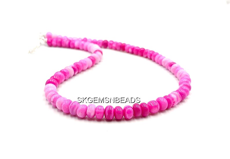 May include: A necklace composed of small, rounded beads in shades of pink and magenta. The beads are strung together, forming a continuous loop. The necklace is displayed against a white background. The text "SKGEMSNBEADS" is visible.