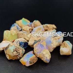 Puede incluir: Una colecci&oacute;n de piedras de &oacute;palo en bruto en varios tonos de blanco, azul y verde. Las piedras son de forma irregular y tienen una textura rugosa y natural. SKGEMSNBEADS