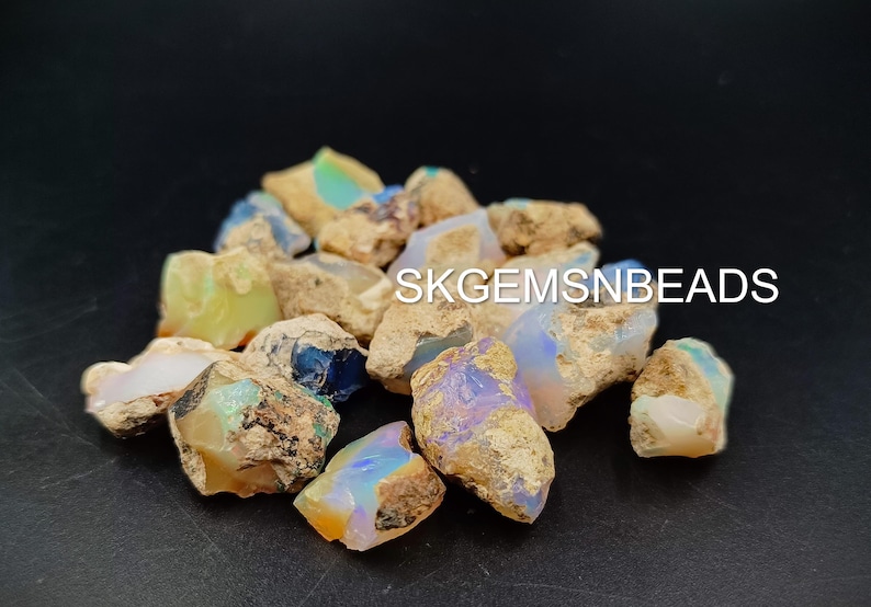 Puede incluir: Una colecci&oacute;n de piedras de &oacute;palo en bruto en varios tonos de blanco, azul y verde. Las piedras son de forma irregular y tienen una textura rugosa y natural. SKGEMSNBEADS