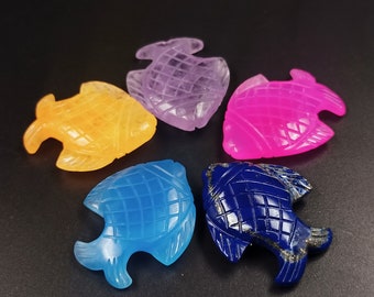 May include: Five carved gemstone fish, each a different color: orange, purple, pink, blue, and dark blue. The fish are all facing the same direction and have a grid pattern carved into their bodies.