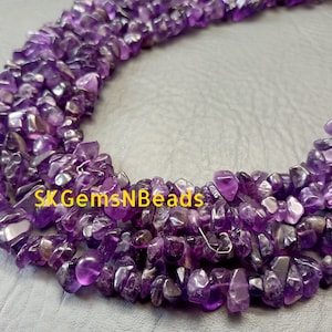 May include: A strand of purple amethyst chip beads. The beads are irregular in shape and have a natural, rough texture. The beads are strung on a clear thread.