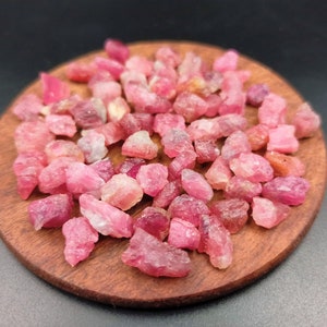 May include: A close-up of a pile of pink ruby rough stones on a wooden surface.