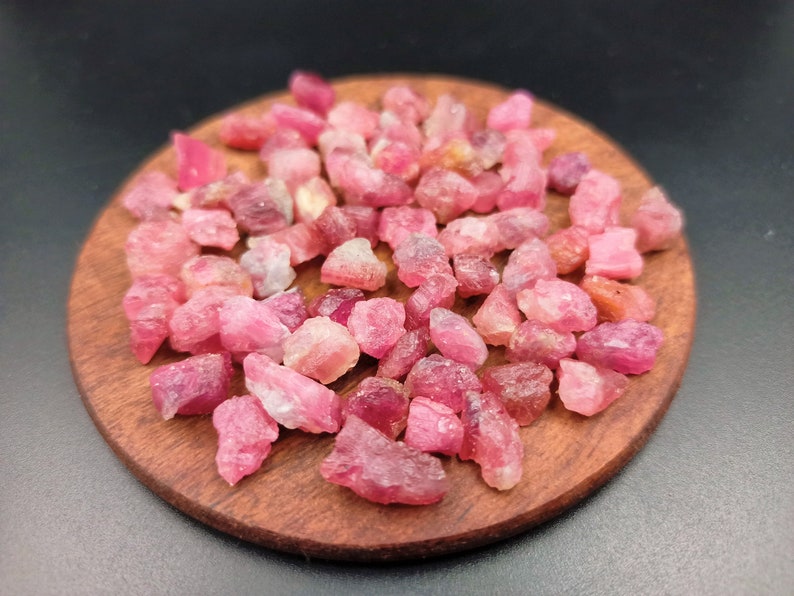 May include: A close-up of a pile of pink ruby rough stones on a wooden surface.