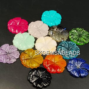 Pode incluir: Uma coleção de formas de flores de pedras preciosas esculpidas em várias cores, incluindo rosa, turquesa, branco, cinza, verde, roxo, amarelo, laranja, preto e azul. As pedras preciosas estão dispostas sobre uma superfície escura.
