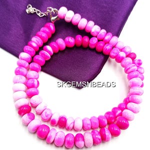 May include: A double strand necklace featuring pink and white beads. The beads are a mix of solid pink and marbled white and pink. The necklace is displayed on a purple cloth. The text "SKGEMSMBEADS" is visible.