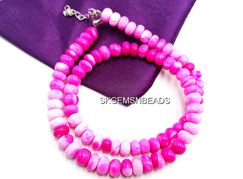 May include: A double strand necklace featuring pink and white beads. The beads are a mix of solid pink and marbled white and pink. The necklace is displayed on a purple cloth. The text "SKGEMSMBEADS" is visible.