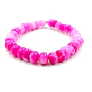 Puede incluir: Un brazalete de cuentas de ágata rosa y blanca. Las cuentas son redondas y tienen un degradado de color de blanco a rosa.
