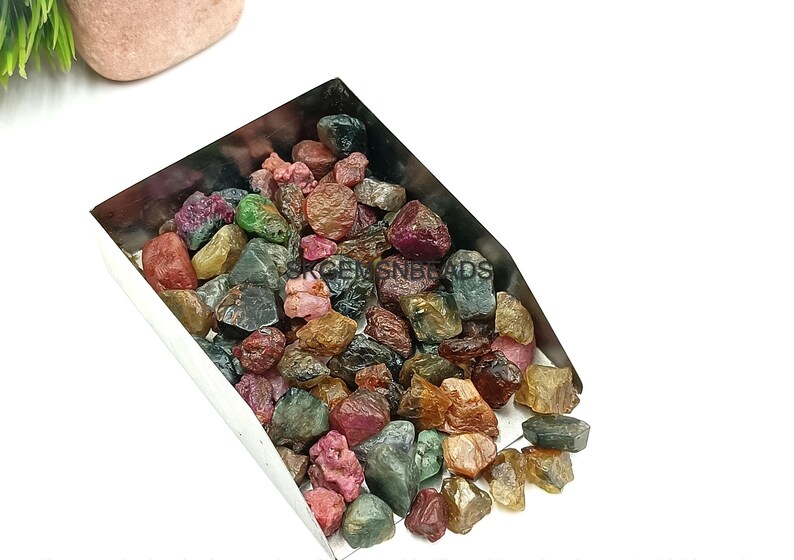 K&ouml;nnte beinhalten: Eine Metallschaufel gef&uuml;llt mit einer Vielzahl von bunten Edelsteinen. Die Edelsteine sind eine Mischung aus Gr&uuml;n, Rot, Rosa und Gelb. Die Edelsteine sind alle roh und unpoliert.