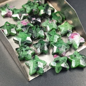 Könnte beinhalten: Eine Sammlung grüner sternförmiger Edelsteine mit roten und schwarzen Einschlüssen. Die Steine sind in einem Metalltablett angeordnet.