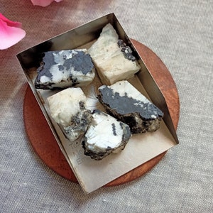 May include: Four pieces of white and black speckled selenite crystal in a silver tray on a wooden coaster.
