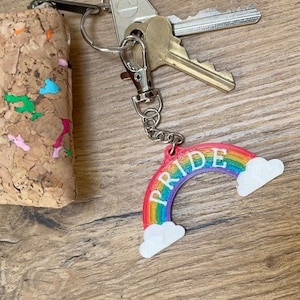May include: A rainbow-colored keychain with the word "PRIDE" written on it. The keychain has two white clouds on either side of the rainbow.