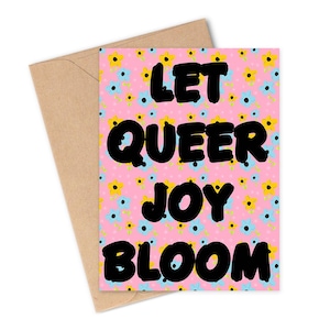Puede incluir: Una tarjeta de felicitación con el texto "LET QUEER JOY BLOOM" en letras negras en negrita. La tarjeta tiene un fondo rosa con un estampado floral de flores azules y amarillas. Se combina con un sobre marrón.