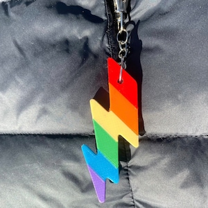 May include: A rainbow-colored lightning bolt keychain with a silver clip. The keychain is made of plastic and has a smooth finish.