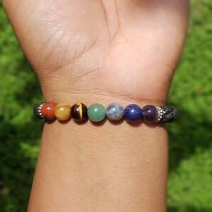 May include: A bracelet with seven colorful beads, including red, orange, yellow, green, blue, indigo, and violet, representing the seven chakras. The bracelet is made with lava rock beads and silver spacers.
