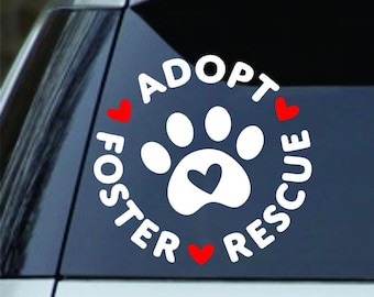 May include: White paw print decal with a heart in the center, surrounded by the words "Adopt, Foster, Rescue" in a circle. Red hearts accent the design. The decal is designed to be applied to a car window.