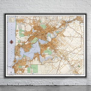 Könnte beinhalten: Vintage-Karte von Perth, Australien, die die Straßen, Wasserwege und Parks der Stadt zeigt. Die Karte ist in Braun, Grün und Blau auf weißem Hintergrund gedruckt. Die Karte ist in Schwarz gerahmt.