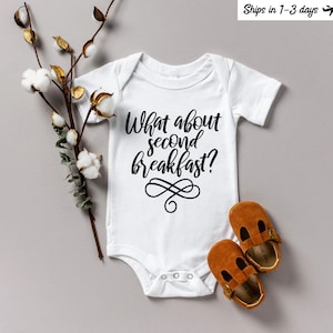 May include: White baby onesie with black text that reads "What about second breakfast?" with a decorative swirl design.