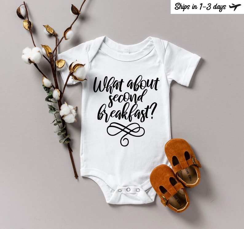 May include: White baby onesie with black text that reads "What about second breakfast?" with a decorative swirl design.
