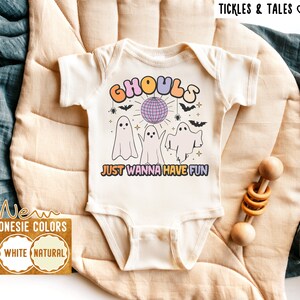 Peut inclure: Combinaison blanche avec un motif de trois fantômes dansant autour d'une boule disco avec le texte "Ghouls Just Wanna Have Fun".