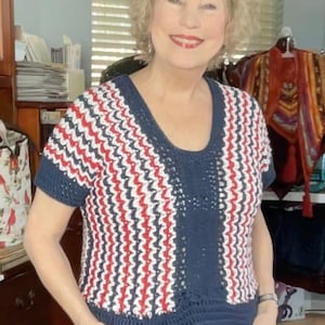 May include: A short-sleeved crochet top in navy blue, red, and white. The top features a scoop neck and a vertical navy blue panel down the center. The crochet pattern creates a zig-zag effect. The top is a handmade garment.