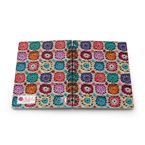 Pode incluir: Um caderno espiral com um padr&atilde;o de croch&ecirc; colorido na capa. A capa apresenta uma variedade de cores, incluindo vermelho, laranja, amarelo, verde, azul, roxo e rosa. O caderno tem um fundo branco e o texto "the hook crochet" est&aacute; impresso na capa.