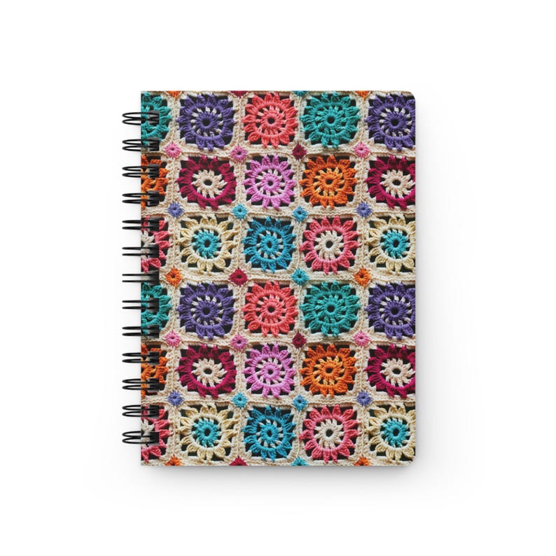 Pode incluir: Um caderno de espiral com uma capa de croch&ecirc; colorida. A capa apresenta um padr&atilde;o repetitivo de quadrados com fios de diferentes cores.