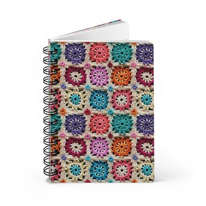 May include: A colorful crocheted notebook cover with a repeating pattern of squares. The squares are made in various colors, including pink, blue, green, orange, and purple.