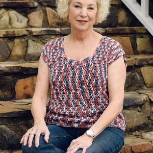 May include: A woman wearing a red, white and blue striped crochet top with blue jeans and a watch on her wrist. She is sitting on stone steps.