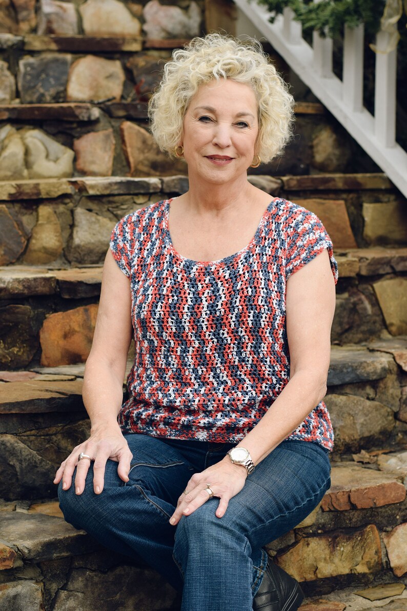 May include: A woman wearing a red, white and blue striped crochet top with blue jeans and a watch on her wrist. She is sitting on stone steps.