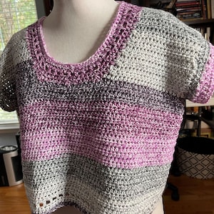 May include: A crocheted top with short sleeves in a striped pattern of purple, gray, and white.