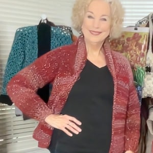 May include: A woman wearing a red and white patterned cardigan with a black v-neck shirt and blue jeans.