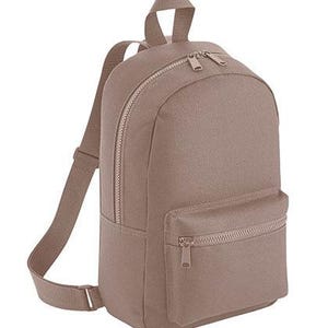 K&ouml;nnte beinhalten: Ein einfarbiger taupefarbener Rucksack mit einem Hauptfach mit zwei Rei&szlig;verschl&uuml;ssen, einer kleineren Rei&szlig;verschlusstasche vorne und verstellbaren Schultergurten. Der Rucksack hat einen Tragegriff oben und besteht aus einem strapazierf&auml;higen Gewebe.