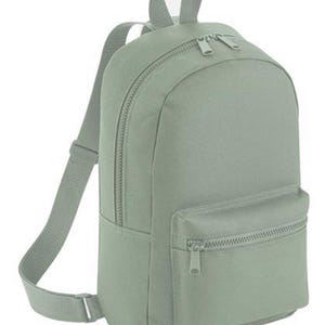 K&ouml;nnte beinhalten: Ein salbeigr&uuml;ner Rucksack mit einem Hauptfach mit zwei Rei&szlig;verschl&uuml;ssen, einer kleineren Rei&szlig;verschlusstasche auf der Vorderseite und verstellbaren Schultergurten. Der Rucksack hat einen Tragegriff oben und besteht aus einem glatten Stoff.