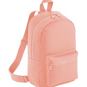 K&ouml;nnte beinhalten: Ein einfarbiger pfirsichfarbener Rucksack mit einem Hauptfach mit Doppelrei&szlig;verschluss, einer kleineren Vordertasche mit einfachem Rei&szlig;verschluss, einem Tragegriff an der Oberseite und verstellbaren Schultergurten aus dem gleichen Material.