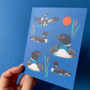 Pode incluir: Um cart&atilde;o azul com um padr&atilde;o repetido de cinco p&aacute;ssaros mergulhadores nadando em um lago azul. Os p&aacute;ssaros s&atilde;o pretos e brancos com olhos vermelhos e bicos laranja. O fundo &eacute; azul s&oacute;lido com um &uacute;nico sol laranja no canto superior direito.