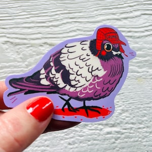May include: A sticker depicting a cartoon pigeon wearing a red hat with the word "GRUMBS". The pigeon has purple and white feathers and is standing on a red puddle. The sticker is on a purple background.