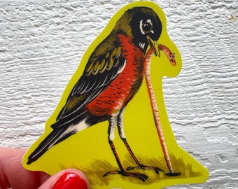 May include: A yellow sticker featuring a stylized illustration of a robin bird with a worm in its beak. The bird has a black head, brown wings, and a red breast. The worm is a light orange color.
