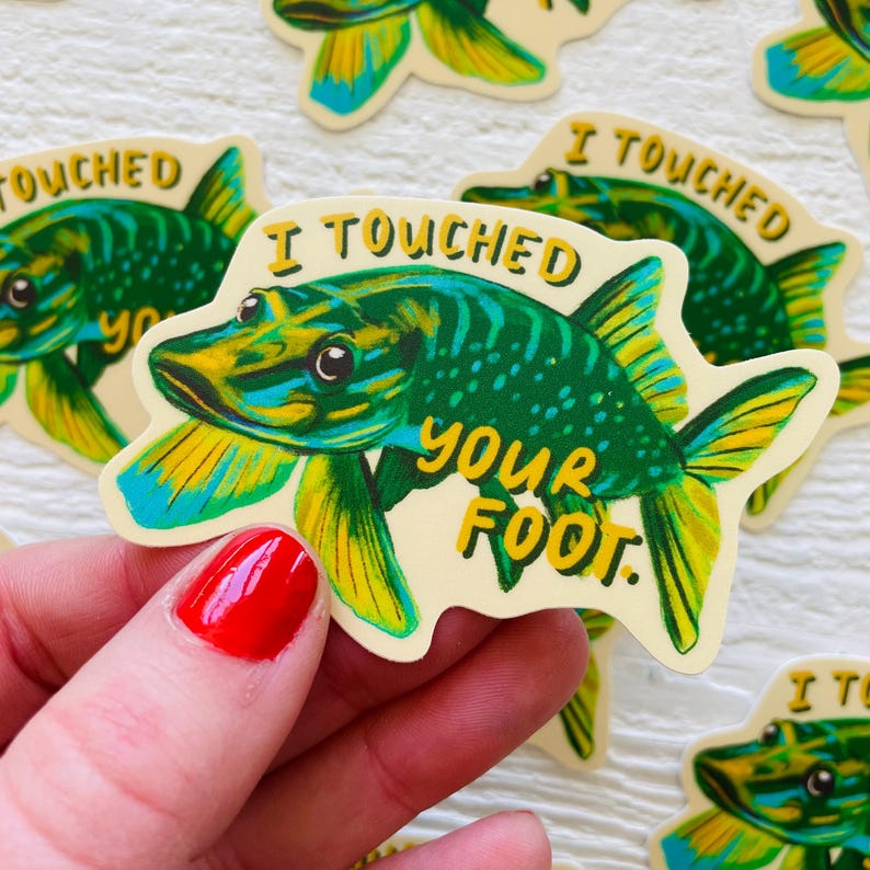 May include: A sticker featuring a green and yellow fish with the text "I touched your foot." The fish has a yellow fin and a blue eye.