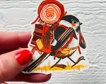 May include: A sticker featuring a bird with a backpack, carrying a large orange lollipop. The bird is black, white, and brown, with a red harness. The backpack is orange and brown, with a yellow and brown mug attached.