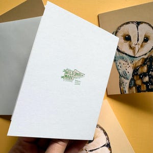 May include: A white folded greeting card featuring a green logo that reads Wild Made Goods Small Business, Est 2020, A Canadian Printed in Ontario. Beside it, a tan card displays a detailed illustration of a brown and white barn owl.