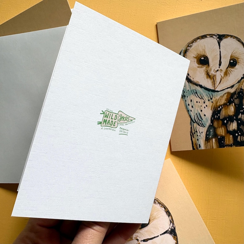 May include: A white folded greeting card featuring a green logo that reads Wild Made Goods Small Business, Est 2020, A Canadian Printed in Ontario. Beside it, a tan card displays a detailed illustration of a brown and white barn owl.